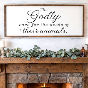 May include: A rectangular wooden sign with the text "The Godly care for the needs of their animals" in black script. The sign is above a wooden mantel decorated with candles, greenery, and bottles. The text "FULLY CUSTOMIZABLE - SIZES, COLORS" is at the bottom.
