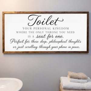 May include: A rectangular wall sign with a dark wood frame and a white background featuring black text that reads: Toilet, YOUR PERSONAL KINGDOM, WHERE THE ONLY THRONE YOU NEED, IS A seat for one., Perfect for those deep, philosophical thoughts, or just scrolling through your phone in peace.