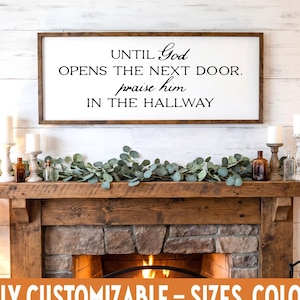 May include: A wooden framed sign with the text "UNTIL God OPENS THE NEXT DOOR. praise him IN THE HALLWAY" hangs above a fireplace. The fireplace is made of stone and wood, with candles and greenery on the mantel. The text "FULLY CUSTOMIZABLE - SIZES, COLORS" is at the bottom.