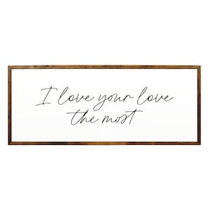 May include: A white wooden sign with a brown frame, featuring the text "I love your love the most" written in black cursive script.