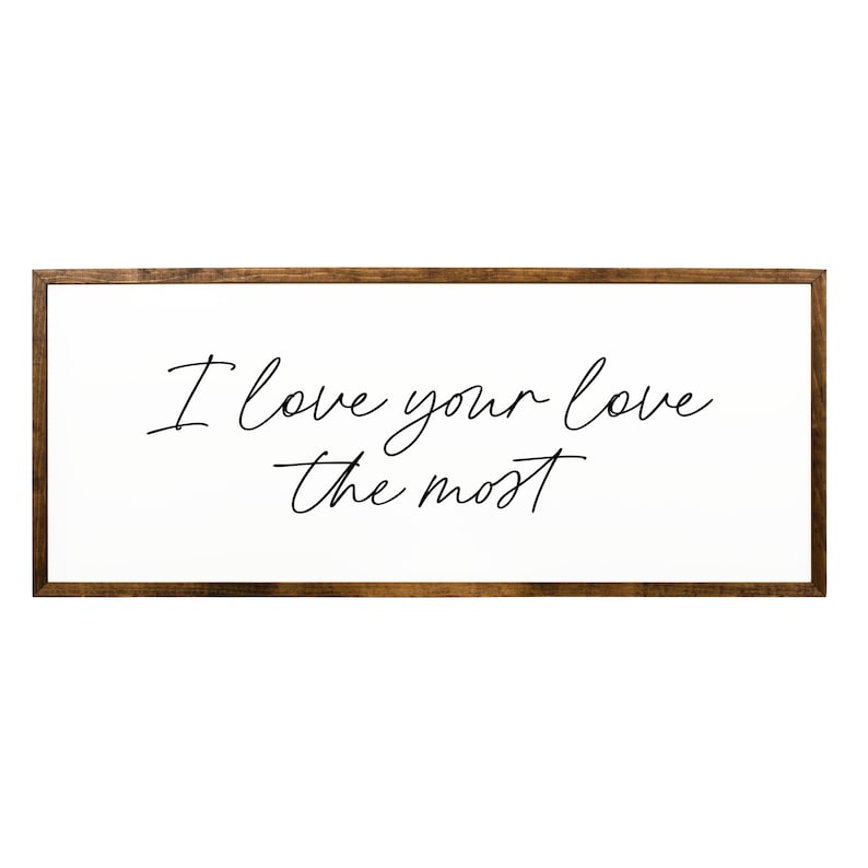 May include: A white wooden sign with a brown frame, featuring the text "I love your love the most" written in black cursive script.