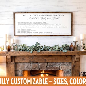 May include: A framed wooden sign displays "The Ten Commandments" in black text. The sign is above a fireplace with candles, bottles, and greenery. The bottom of the image has the text "FULLY CUSTOMIZABLE - SIZES, COLORS".