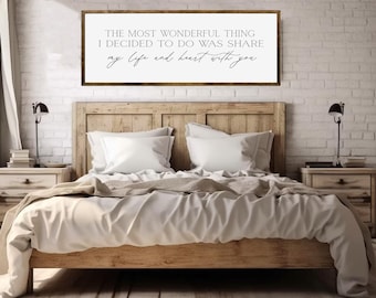 May include: A wooden framed sign with the text "THE MOST WONDERFUL THING I DECIDED TO DO WAS SHARE my life and heart with you" displayed above a bed. The bed has a wooden frame, white bedding, and two nightstands with lamps.