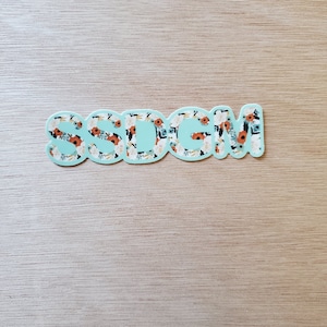 Peut inclure: Un autocollant avec le mot "SSDM" en lettres blanches avec un motif floral sur un fond bleu clair.
