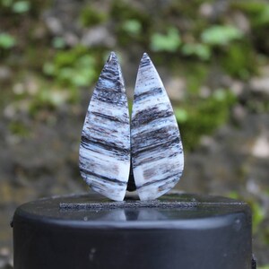 May include: Two teardrop-shaped, white and black striped stone earrings. The earrings are displayed on a black stand.