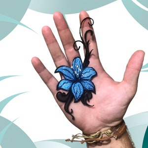 Pode incluir: Uma flor bordada azul com detalhes brancos e caules pretos em uma mão.
