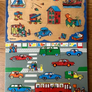 Op de afbeelding: Twee houten legpuzzels. De bovenste puzzel toont een zeilboot, trein, bal, schip, huis, kraan, auto, clown en andere vormen. De onderste puzzel toont auto's, een bus en mensen die een straat oversteken. De puzzels zijn gemaakt door Simplex.
