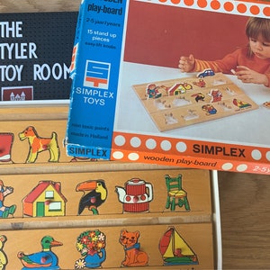 May include: A wooden play-board with colourful wooden pieces for children aged 2-5 years. The board features a variety of images, including a house, a duck, a cat, a flower, a teapot, a chair, a toucan, a boot, a dog, and a bear. The board is made by Simplex Toys and is made in Holland.