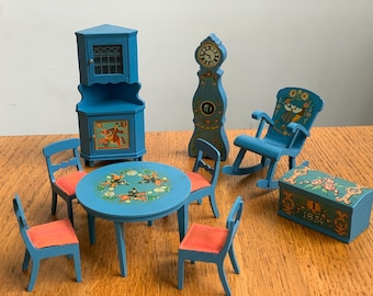 May include: A set of blue and white painted wooden dollhouse furniture, including a rocking chair, a table with four chairs, a hutch, a grandfather clock, and a chest. The furniture is decorated with floral and animal motifs.