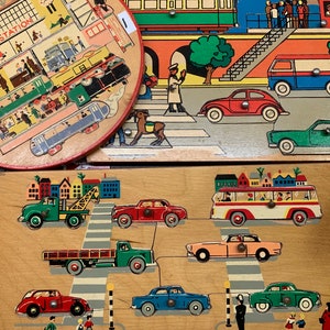 Op de afbeelding: Drie houten speelgoedpuzzels met een treinstation, auto's en een bus. De puzzels zijn genummerd 1, 2 en 3. De treinstationpuzzel heeft een rood, wit en blauwe trein. De auto-puzzel heeft een rode, blauwe en groene auto. De bus-puzzel heeft een gele bus met een rood dak.