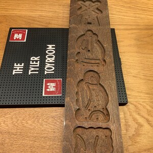 May include: A wooden cookie cutter with four different designs: a windmill, a snowman, a Santa Claus, and a gingerbread man. The cookie cutter is brown and has a rustic look.