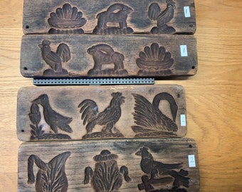 May include: Three antique wooden cookie molds with carved designs. The top mold features a rooster, a rabbit, and a shell. The middle mold features a bird, a rooster, and a swan. The bottom mold features a bird, a plant, and a bird.