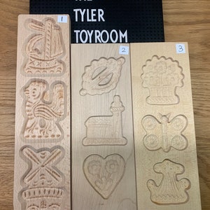 May include: Three wooden cookie cutters with different designs. The first cutter has three designs: a windmill, a rooster, and a building with a pointed roof. The second cutter has four designs: a heart, a church, a leaf, and a star. The third cutter has four designs: a butterfly, a basket of flowers, a crown, and a mushroom.
