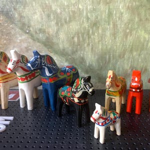May include: A collection of eight hand-painted wooden horses, known as Dala horses, in various colours and designs. The horses are traditional Swedish folk art and are often used as decorations.