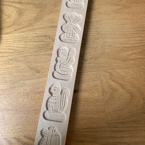 May include: A wooden cookie mold with five different designs: a squirrel, a windmill, a bird, a rooster, and a fish. The mold is made of light brown wood and has a smooth surface.