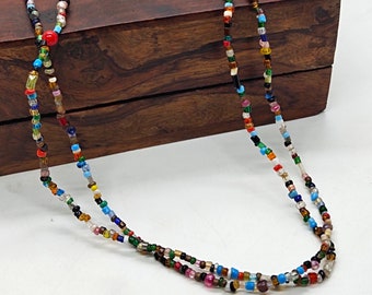 May include: A multi-colored beaded necklace with a variety of small, round beads in shades of red, blue, green, yellow, and brown. The necklace is made of two strands of beads and is lying on a wooden surface.
