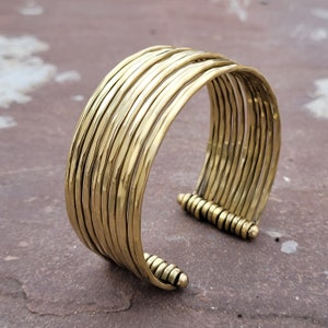 May include: A gold-toned hammered metal bangle bracelet with multiple layers. The bracelet is open and has a hammered texture.