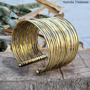 May include: A gold-toned bangle bracelet made of multiple thin, hammered metal bands. The bracelet is open and has a clasp on the side.