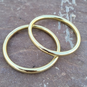 May include: Two gold-coloured metal bangles, one slightly larger than the other, are stacked on top of each other. The bangles are smooth and shiny.