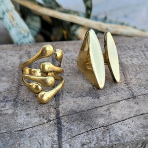 May include: Two gold rings. One ring has a unique design with multiple rounded shapes. The other ring is a simple oval shape.