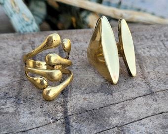 May include: Two gold rings. One ring has a unique design with multiple rounded shapes. The other ring is a simple oval shape.