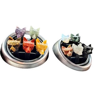 May include: Two car air vent diffusers with decorative, carved fox heads in various colors. The foxes are made of different types of stone, including tiger's eye, amethyst, and jade. The diffusers are silver and black.