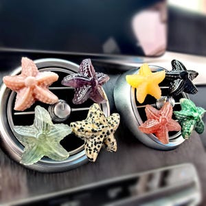 Può includere: Una collezione di profumatori per auto a forma di stella marina colorata. I profumatori sono in vari colori, tra cui rosa, viola, giallo, nero, rosso, verde e maculato. Sono progettati per agganciarsi alle bocchette dell'aria condizionata dell'auto.