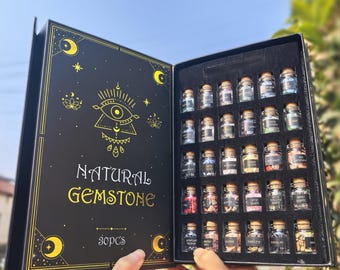 Könnte beinhalten: Eine schwarze Box mit goldfarbenem Schriftzug "NATURAL GEMSTONE" und "30pcs". Sie enthält 30 kleine Glasflaschen mit Korken, jede gefüllt mit einem anderen Edelstein. Die Box hat ein himmlisches Design mit Monden und Sternen.