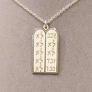 May include: A silver chain necklace with a pendant shaped like two tablets with Hebrew text inscribed on them.