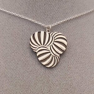 May include: A silver necklace with a pendant shaped like three overlapping circles with a striped pattern.