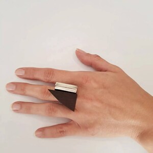 Puede incluir: Un anillo geométrico plateado y marrón con un diseño rectangular y triangular.