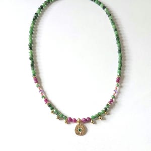 Peut inclure: Collier de perles composé de pierres précieuses vertes et roses. Le pendentif doré est orné d'une pierre verte. Les perles sont enfilées sur un fil délicat. Le collier est présenté sur fond blanc.