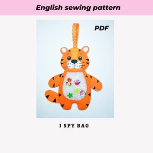 May include: A PDF sewing pattern for an orange and black tiger-shaped I Spy bag. The bag has a clear plastic window on the front, and the pattern includes instructions for making the bag.