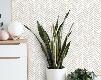 May include: A modern interior scene featuring a white cabinet, wooden stools, and potted plants. The background is a wallpaper with a beige chevron pattern. A snake plant and other greenery add a natural touch to the decor.