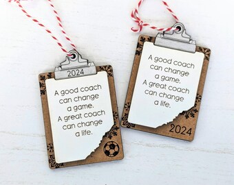 May include: Two brown wooden clipboard ornaments with a white background and black text. The text reads "A good coach can change a game. A great coach can change a life." The ornaments are decorated with snowflakes and the year 2024. One ornament has a football graphic.