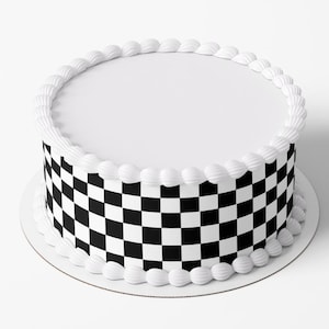 May include: A round cake with a white top and a black and white chequered pattern around the sides. The cake is decorated with white icing around the top and bottom edges, and sits on a white cake board.