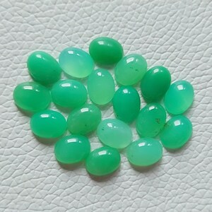 May include: A collection of 18 oval-shaped green gemstones. The stones are smooth and polished, with a translucent appearance.