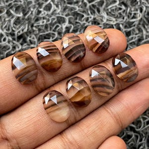 May include: Eight faceted oval-shaped brown and white agate gemstones with a striped pattern.