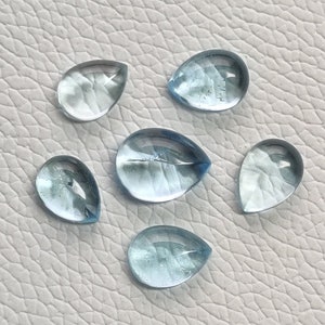 May include: Six teardrop-shaped aquamarine gemstones, each with a light blue color and a translucent appearance.
