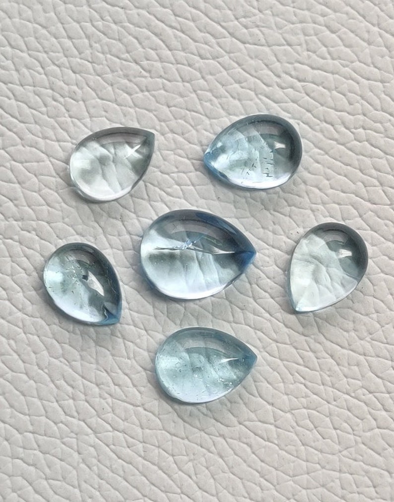 May include: Six teardrop-shaped aquamarine gemstones, each with a light blue color and a translucent appearance.