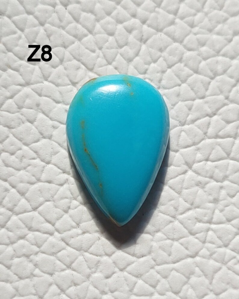 May include: A teardrop-shaped turquoise gemstone with a blue-green color and brown veins. The stone is set against a white background.