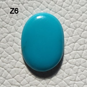 May include: A bright turquoise oval cabochon gemstone. The stone is smooth and polished, with a slight sheen.