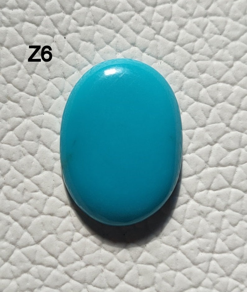 May include: A bright turquoise oval cabochon gemstone. The stone is smooth and polished, with a slight sheen.