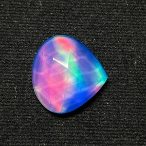 Op de afbeelding: Een regenboogkleurige, traanvormige edelsteen met een blauw, roze en groen kleurpatroon.