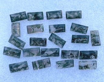 May include: A collection of 19 green moss agate gemstones, each cut into a rectangular shape. The stones have a translucent, cloudy appearance with green moss-like inclusions.