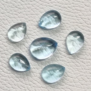 May include: Six teardrop-shaped aquamarine gemstones, each with a light blue color and a smooth, polished surface.