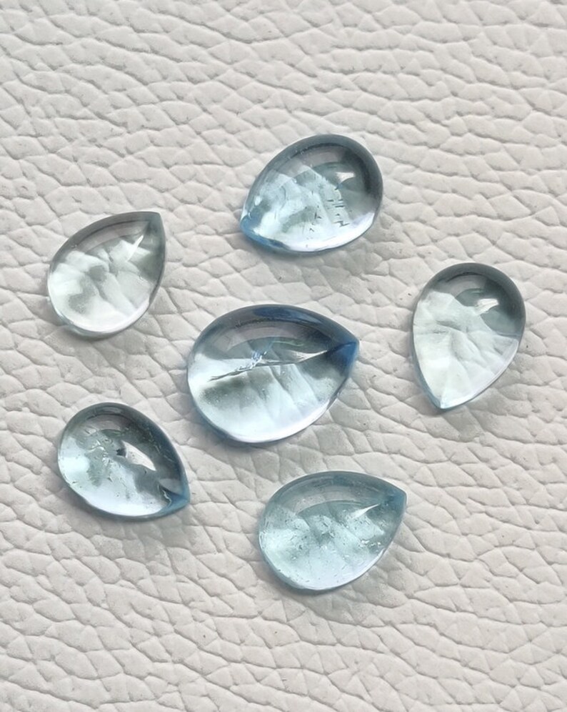 May include: Six teardrop-shaped aquamarine gemstones, each with a light blue color and a smooth, polished surface.