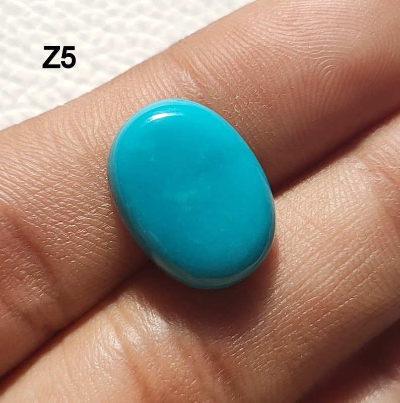 May include: A bright turquoise oval cabochon gemstone. The stone is smooth and polished, with a slight sheen.