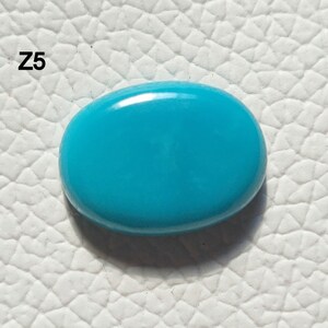 May include: A bright turquoise oval cabochon gemstone. The stone is smooth and polished, with a slight sheen.