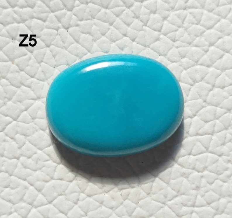 May include: A bright turquoise oval cabochon gemstone. The stone is smooth and polished, with a slight sheen.